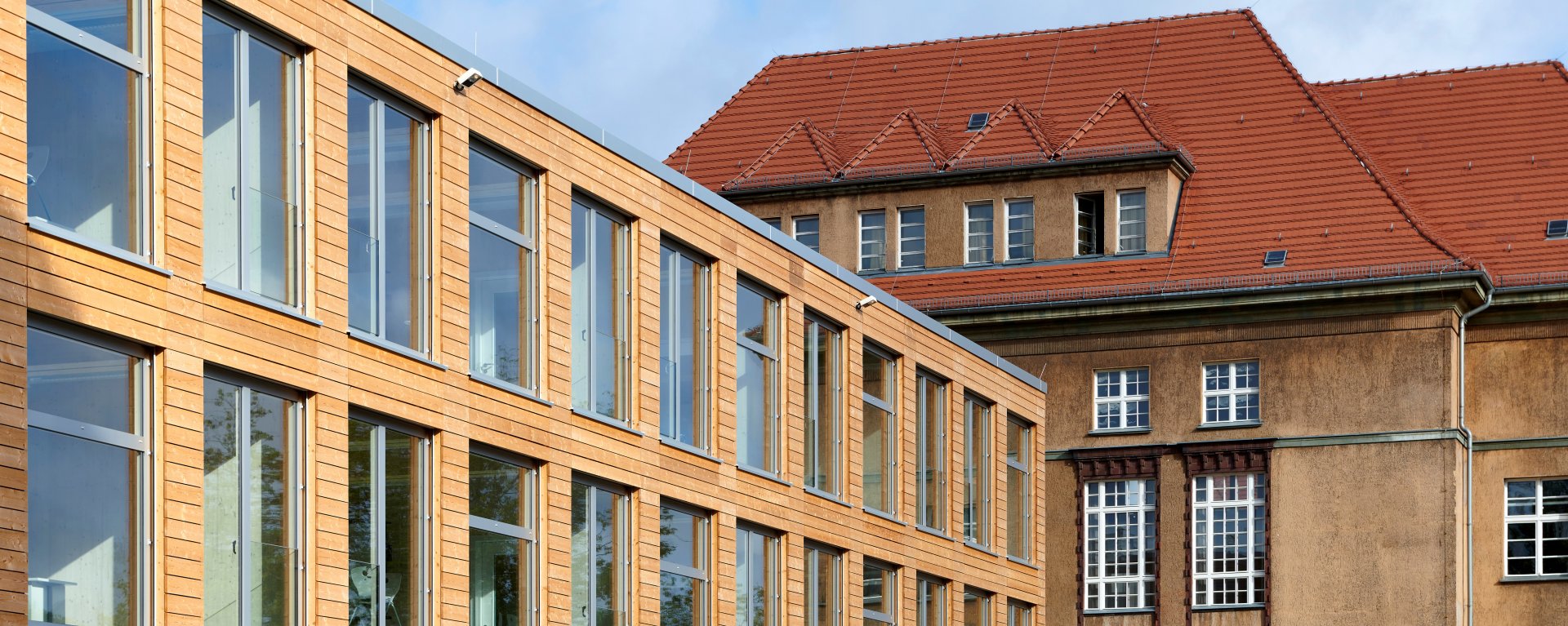 Müggelsee-Schule, a new building with flat roof and wooden facade is connected to a historic building facade